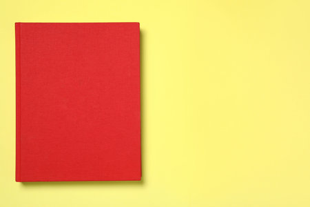 Book with red cover on yellow background, top view. Space for textの写真素材