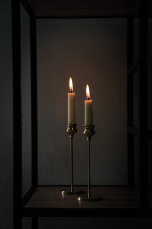 Burning candles on shelving unit in dark roomの写真素材