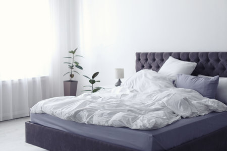 Modern bed with crumpled blanket and pillows indoorsの写真素材