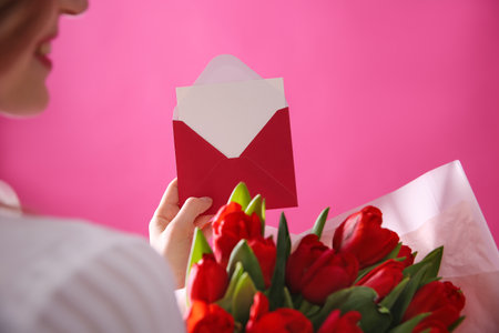 Woman holding envelope with blank greeting card and bouquet of tulips on pink background, closeupの写真素材