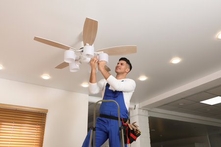 Electrician changing light bulb in ceiling fan indoorsの写真素材