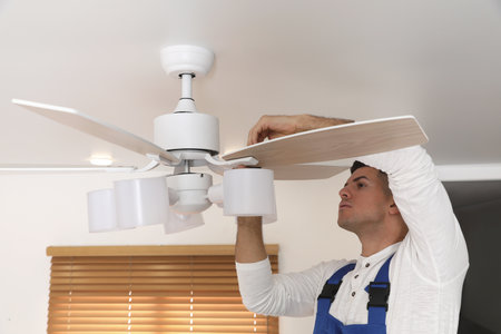 Electrician repairing ceiling fan with lamps indoorsの写真素材