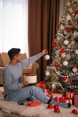 Handsome man decorating Christmas tree at homeの写真素材