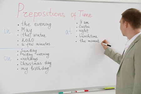 English teacher giving lesson on prepositions of time near whiteboard in classroomの写真素材