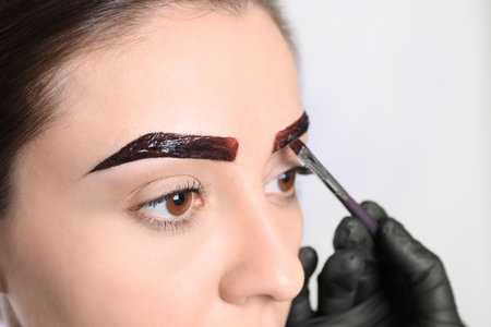 Beautician applying tint during eyebrows correction procedure on light background, closeupの写真素材