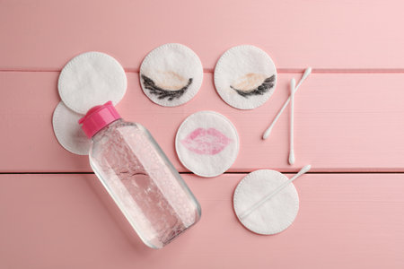 Dirty cotton pads, swabs and micellar cleansing water on pink wooden background, flat layの写真素材
