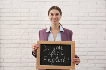 Teacher holding small chalkboard with inscription Do You Speak English? near white brick wallの写真素材
