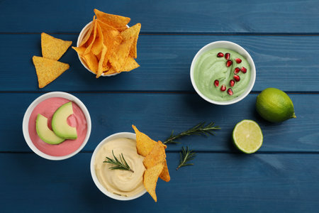 Different kinds of tasty hummus served with nachos on blue wooden table, flat layの写真素材