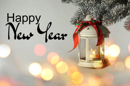 Happy New Year. Christmas lantern with candle hanging on fir tree branch against light background.の写真素材