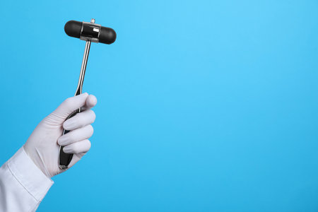 Doctor holding reflex hammer on light blue background, closeup with space for text. Nervous system diagnosticの写真素材