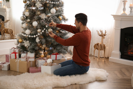 Man decorating Christmas tree in beautiful room interiorの写真素材