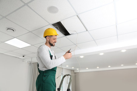 Electrician with pliers repairing ceiling wiring indoorsの写真素材