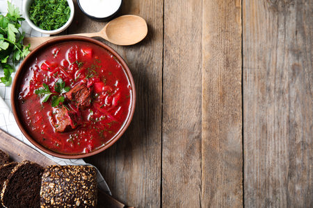 Stylish brown clay bowl with Ukrainian borsch on wooden table, flat lay. Space for text