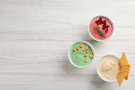 Different kinds of tasty hummus on white wooden table, flat lay. Space for text