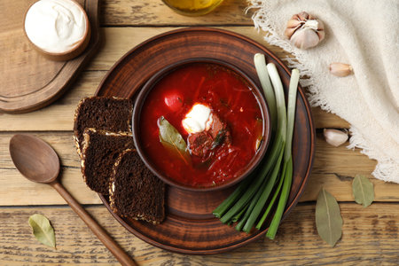 Clay bowl with Ukrainian borsch served on wooden table, flat lay