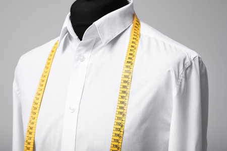 White shirt with tailor's measuring tape on mannequin against gray background, closeup