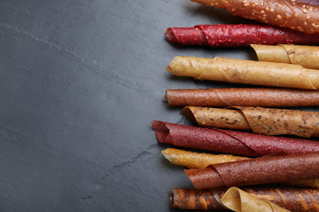 Delicious fruit leather rolls on black table, flat lay. Space for text