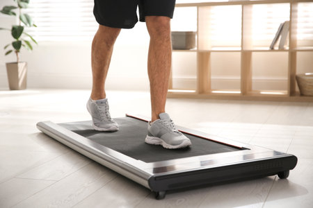 Sporty man training on walking treadmill at home, closeup