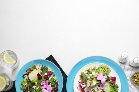 Fresh spring salads with flowers served on white table, flat lay. Space for textの写真素材