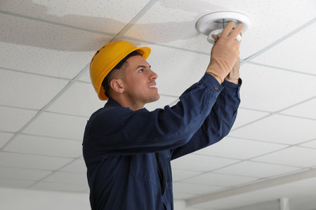 Electrician in uniform repairing ceiling lamp indoorsの写真素材