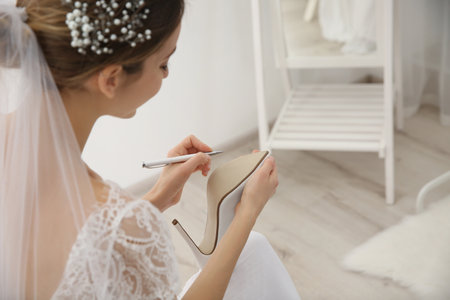 Young bride writing on her shoe indoors, closeup. wedding superstitionの写真素材