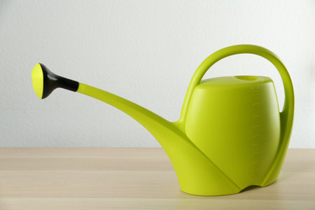 Green plastic watering can on wooden table against white backgroundの写真素材