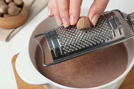 Woman grating nutmeg into cacao at table, closeupの写真素材