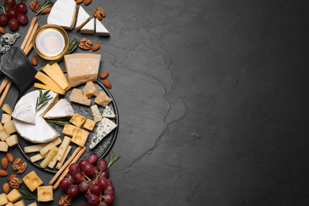Cheese plate with honey, grapes and nuts on black table, flat lay. Space for textの写真素材