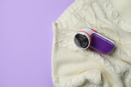 Modern fabric shaver and woolen sweater on purple background, top view. Space for textの写真素材