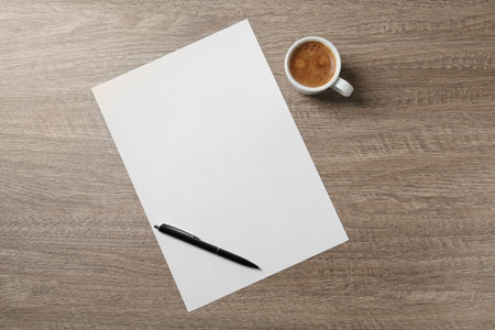 Blank paper sheet, pen and cup of coffee on wooden table, flat lay. Space for textの写真素材