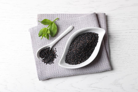 Black sesame seeds and green leaf on white table, top viewの写真素材