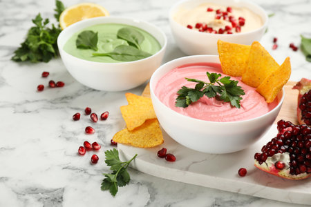 Bowl of delicious pink hummus with tortilla chips and parsley on white marble table