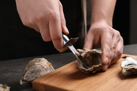 Man opening fresh oyster with knife at gray table, closeupの写真素材