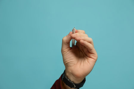 Left-handed man holding pen on light blue background, closeup. Space for textの写真素材