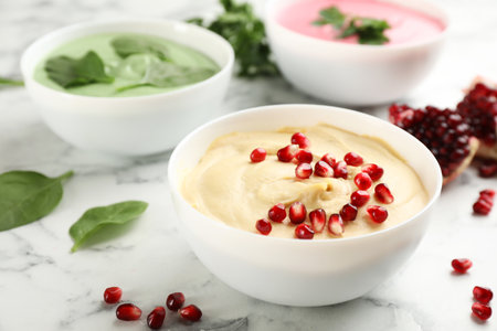 Bowl of delicious classic hummus with pomegranate seeds on white marble tableの写真素材