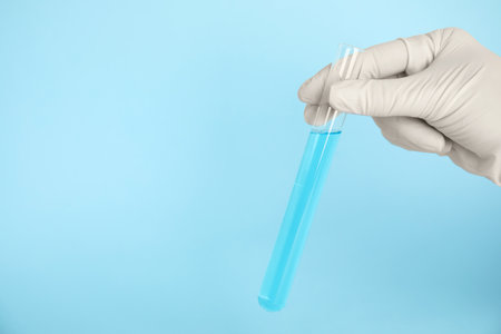 Scientist holding test tube with liquid on turquoise background, closeup. Space for text