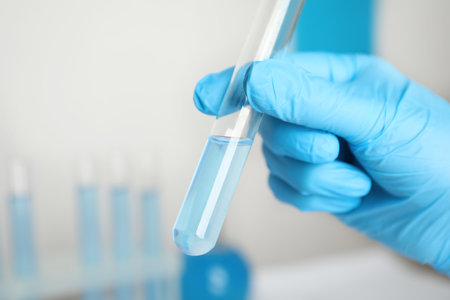 Scientist holding test tube with liquid in laboratory, closeup
