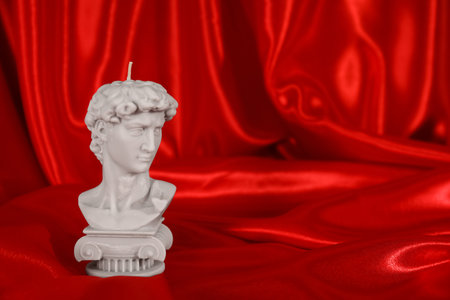 Beautiful David bust candle on red satin. Space for textの写真素材