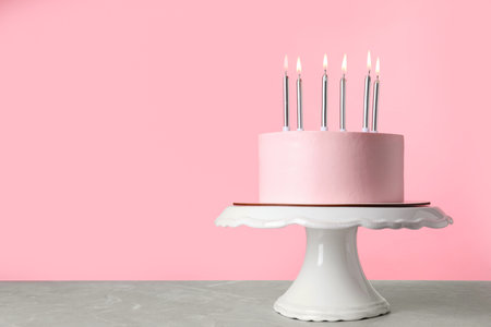 Birthday cake with burning candles on table against pink background, space for textの写真素材