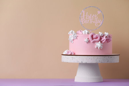 Beautifully decorated birthday cake on violet table near beige wall, space for textの写真素材