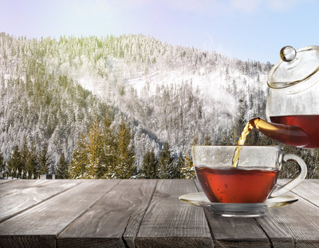 Pouring tea into glass cup on wooden table and beautiful winter landscape on backgroundの写真素材