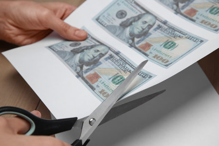 Counterfeiter cutting dollar banknotes with scissors at wooden table, closeup. fake money conceptの写真素材