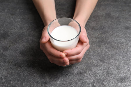Woman holding glass of milk at gray table, closeupの写真素材