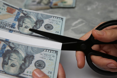 Counterfeiter cutting dollar banknotes with scissors at gray marble table, closeup. fake moneyの写真素材