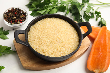 Uncooked rice in wok and products on white wooden tableの写真素材