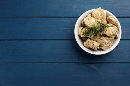 Dehydrated soy meat chunks with dill in bowl on blue wooden table, top view. Space for textの写真素材