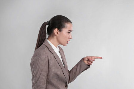 Emotional woman in suit pointing with index finger on light gray backgroundの写真素材