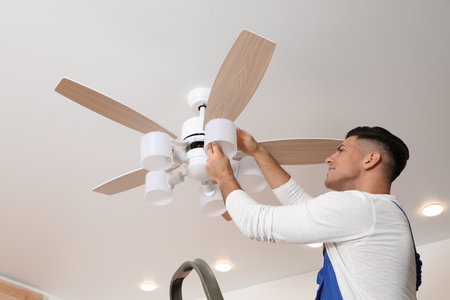 Electrician changing light bulb in ceiling fan indoorsの写真素材