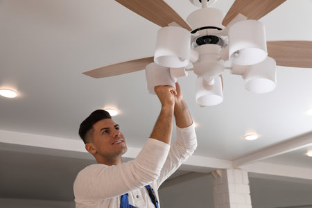 Electrician changing light bulb in ceiling fan indoorsの写真素材