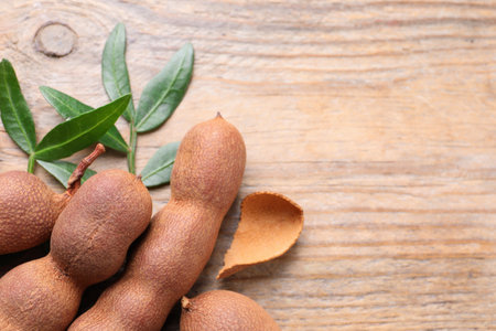 Ripe tamarinds and fresh leaves on wooden table, flat lay. Space for textの写真素材